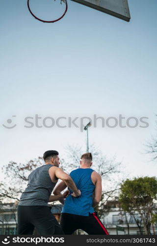 Portrait of two young friends playing basketball and having fun on court outdoors. Sports concept.