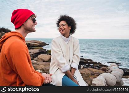 Portrait of two young friends spending good time together and having a conversation while sitting with the sea in the background.