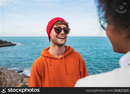 Portrait of two young friends spending good time together and having fun with the sea in the background.