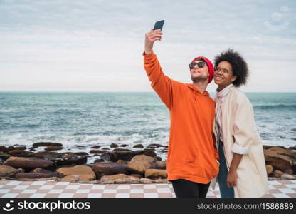 Portrait of two young friends spending good time together and taking a selfie with smartphone outdoors against the sea.