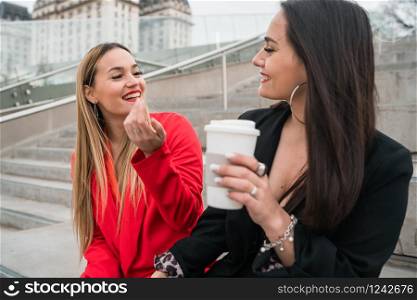 Portrait of two young friends spending good time together while sitting outdoors at the street. Lifestyle and friendship concepts.
