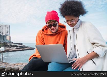Portrait of two young friends spending some time together and using a laptop outdoors. Technology concept.