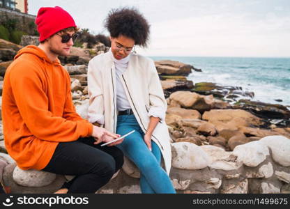 Portrait of two young friends spending some time together and using digital tablet outdoors. Technology concept.