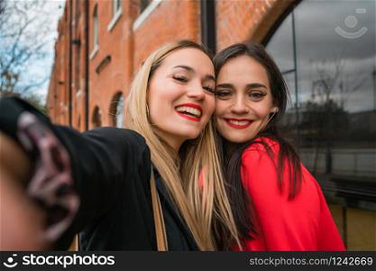 Portrait of two young friends taking a selfie outdoors at the street. Lifestyle and friendship concepts.