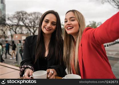 Portrait of two young friends taking a selfie together while sitting at coffee shop. Lifestyle and friendship concept.