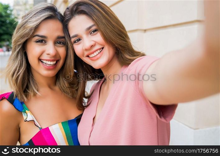 Portrait of two young friends taking a selfie while standing outdoors on the street. Urban concept.