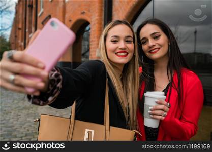 Portrait of two young friends taking a selfie with mobile phone at the street. Lifestyle and friendship concepts.