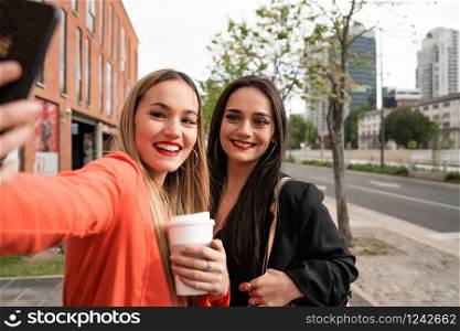 Portrait of two young friends taking a selfie with mobile phone at the street. Lifestyle and friendship concepts.