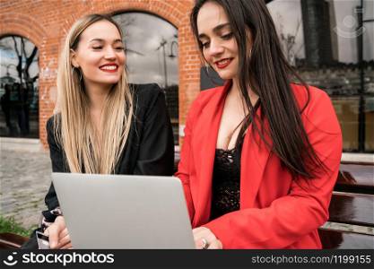 Portrait of two young friends using a laptop while sitting outdoors. Friendship and lifestyle concept.
