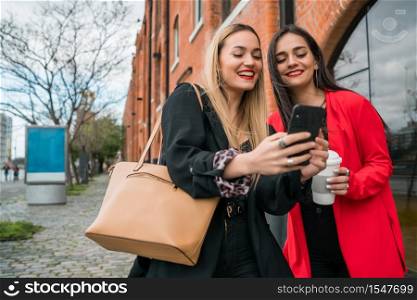 Portrait of two young friends using their mobile phone outdoors at the street. Lifestyle and friendship concepts.