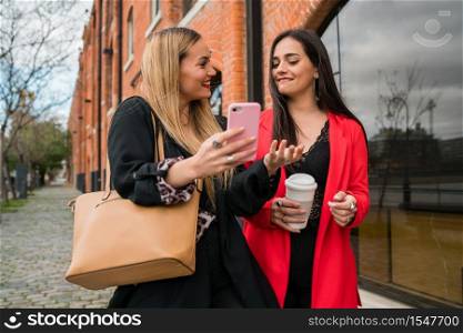 Portrait of two young friends using their mobile phone outdoors at the street. Lifestyle and friendship concepts.