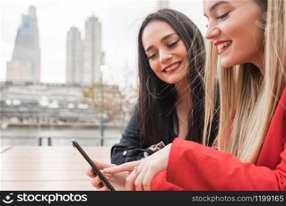 Portrait of two young friends using their mobile phone while sitting at coffee shop. Lifestyle and friendship concept.