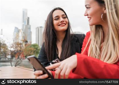 Portrait of two young friends using their mobile phone while sitting at coffee shop. Lifestyle and friendship concept.