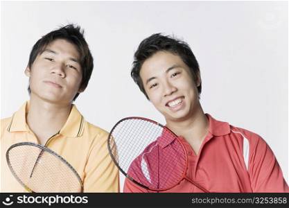 Portrait of two young men holding badminton rackets and smiling