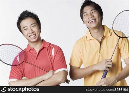 Portrait of two young men holding badminton rackets and smiling