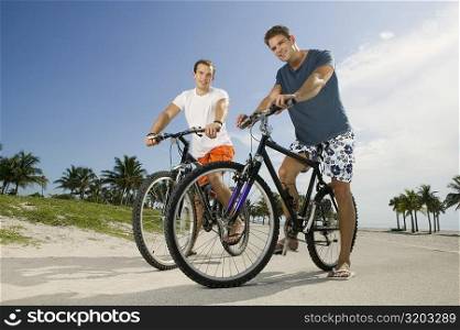Portrait of two young men holding bicycles