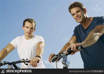 Portrait of two young men smiling and holding bicycles