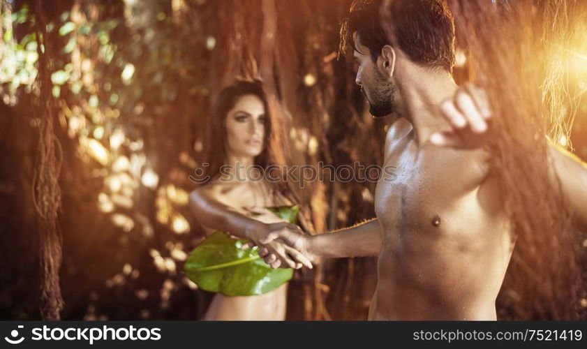 Portrait of two young, nude lovers walking among tropical trees