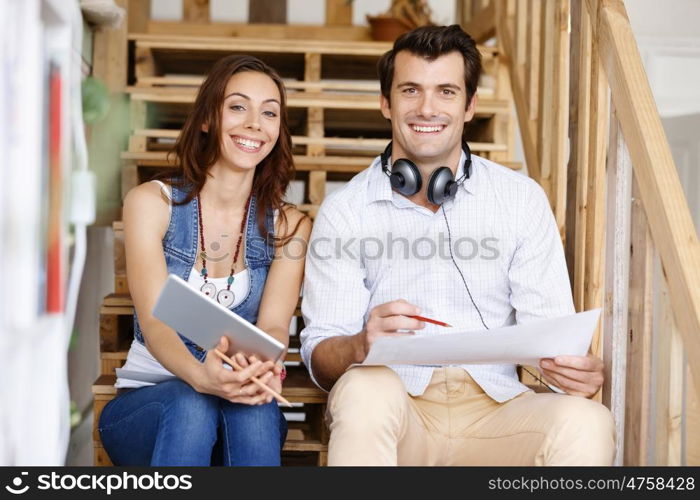 Portrait of two young people sitting at the stairs in office. Portrait of two young people sitting at the stairs in office talking