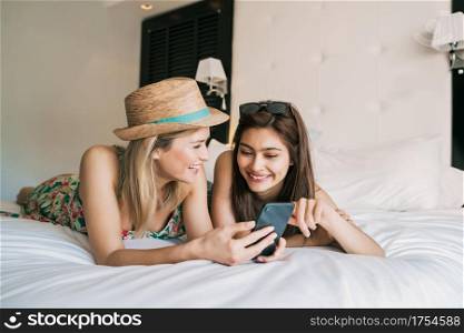 Portrait of two young travelers friends spending some time and using mobile phone at hotel room. Travel and lifestyle concept.