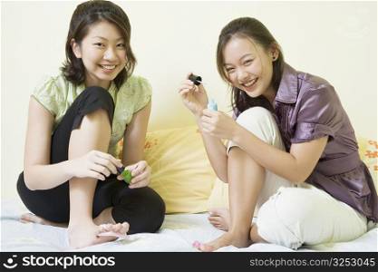 Portrait of two young women applying nail polish on their toenails