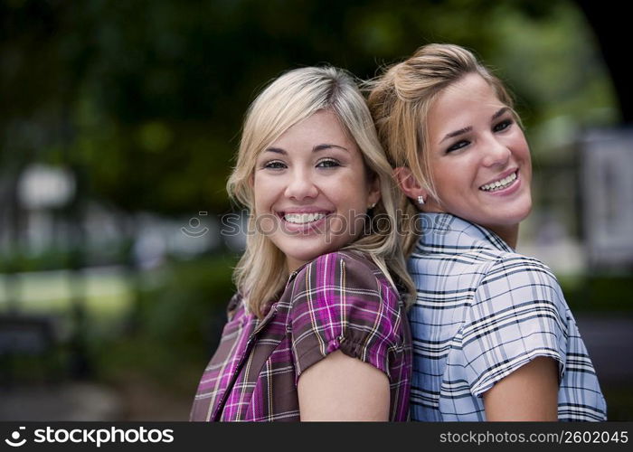 Portrait of two young women back to back and smiling