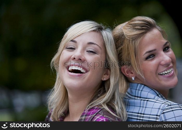 Portrait of two young women back to back and smiling
