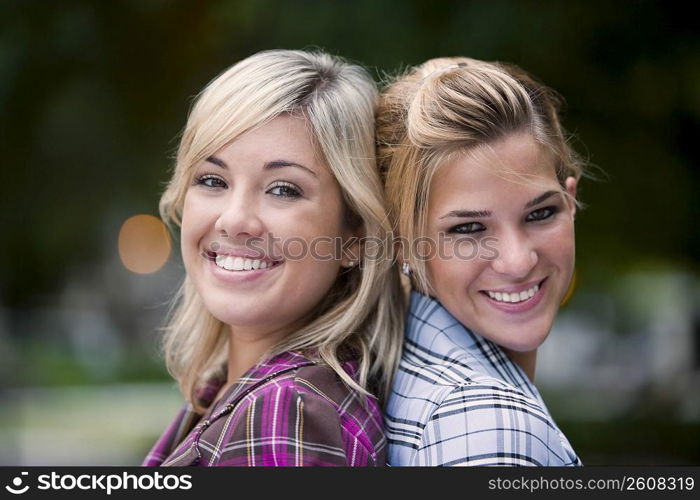 Portrait of two young women back to back and smiling