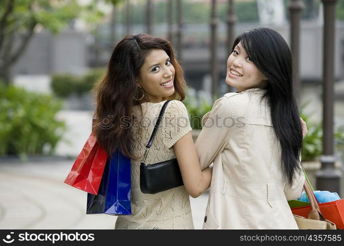 Portrait of two young women carrying shopping bags and smiling