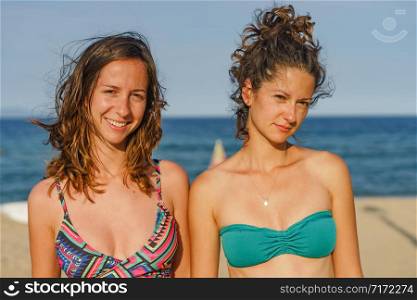 Portrait of two young women female girls friends or sisters in sunny day wearing bikini swim suit in front of the sea