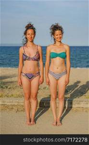 Portrait of two young women female girls friends or sisters in sunny day wearing bikini swim suit in front of the sea on the beach