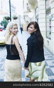 Portrait of two young women holding hands and walking on the sidewalk