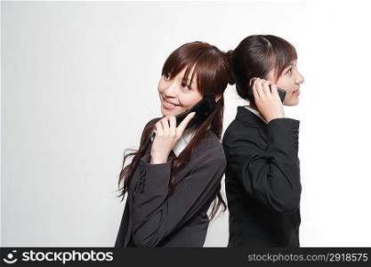 Portrait of two young women in business suit using mobile phones