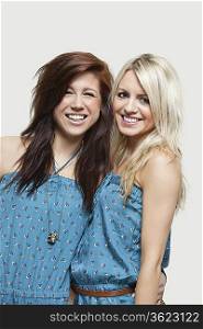 Portrait of two young women in similar jump suits smiling over gray background
