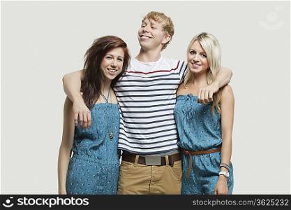 Portrait of two young women in similar jumpsuits standing with happy male friend over gray background