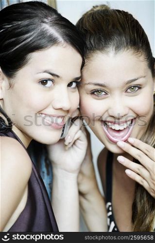 Portrait of two young women listening to a mobile phone and smiling