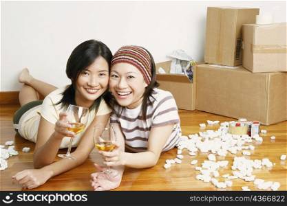 Portrait of two young women lying on the floor and holding glasses of whiskey