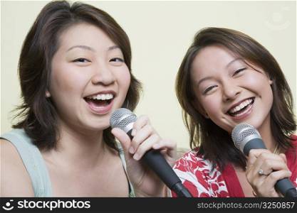 Portrait of two young women singing together into microphones