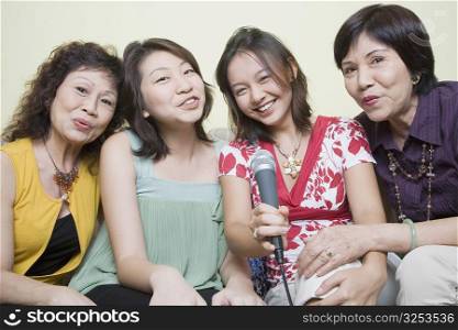Portrait of two young women singing with their grandmothers into microphones