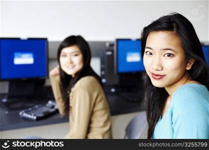 Portrait of two young women sitting in front of computers and smiling