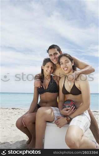 Portrait of two young women sitting on an ice box with a young man standing behind them