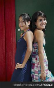 Portrait of two young women standing back to back and smiling
