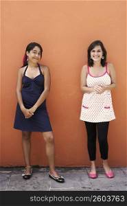 Portrait of two young women standing in front of a wall
