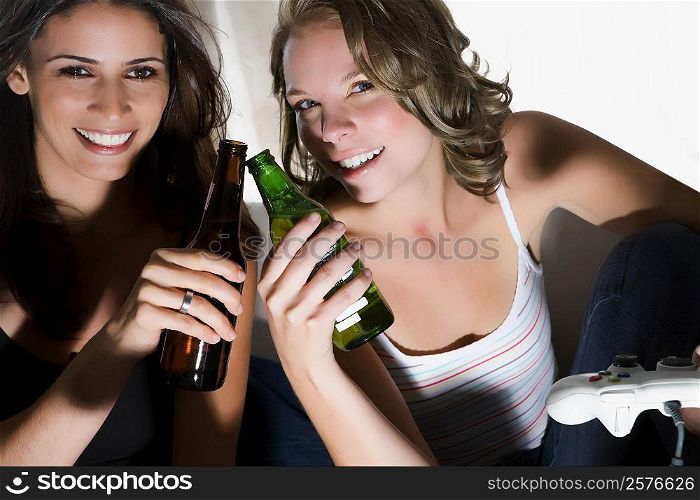 Portrait of two young women toasting with beer bottles and smiling