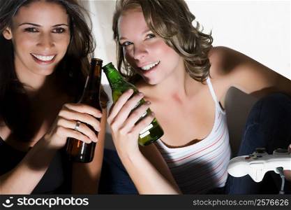 Portrait of two young women toasting with beer bottles and smiling
