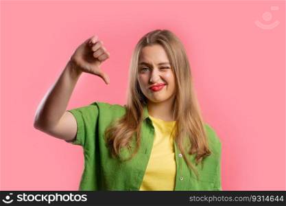Portrait of unhappy european woman condemns with sign of dislike. Young millennial lady expressing discontent with showing thumbs-down gesture on pink studio background.. Pretty woman with sign of dislike. Young millennial girl showing thumbs-down