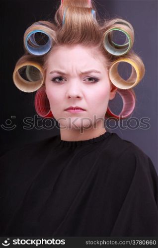 Portrait of unhappy woman in beauty salon. Displeased blond girl with hair curlers rollers by hairdresser. Hairstyle.