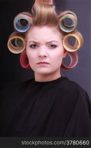 Portrait of unhappy woman in beauty salon. Displeased blond girl with hair curlers rollers by hairdresser. Hairstyle.