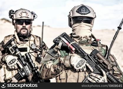 Portrait of United States Marine Corps soldiers in helmet, and ballistic glasses, wearing camouflage uniform and load, carrier, armed with service rifles. Marine riders in combat conditions in desert. Marine riders at secret operation in desert area