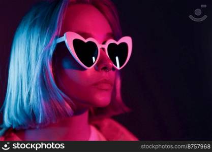 Portrait of unusual beautiful glamour and fashion girl with heat-shaped sunglasses on studio background. Young woman in pink and violet neon light. Portrait of unusual beautiful glamour and fashion girl with heat-shaped sunglasses on studio background. Young woman in pink and violet neon light. 